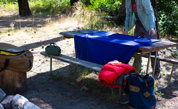 A Large Shepherd's Wool Utility Cloth in Neela Blue spread out onto a picnic table at a campsite.